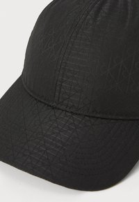 Black cap featuring a textured pattern of intersecting lines, with a curved brim and stitched detailing along the edges.