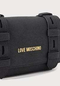 Schwarze Love Moschino Handtasche mit goldfarbener Logo-Schriftzug und zwei dekorativen Riemen an der Vorderklappe.