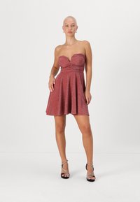 Õlgadeta, särav roosa kleit, millel on ümber kehakujuline vest ja sirge seelik. Sile tekstuur, kaste rinna juures. Mustad rihmadega kontsad.