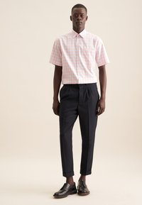 Korte mouw, roze en blauwe geblokte shirt met een button-down kraag en een borstzak, gecombineerd met op maat gemaakte zwarte broeken en zwarte schoenen.