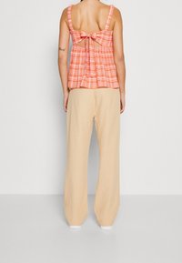 Top sin mangas de cuadros rojos y blancos con un lazo en la parte posterior, combinado con pantalones de pierna ancha beige. Tejido suave y corte relajado.