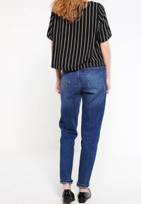 Top a maniche corte a righe bianche e nere, abbinato a jeans in denim blu a vita media. I jeans hanno una vestibilità affusolata e orli arrotolati. Scarpe nere.