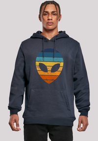 Navy hooded sweatshirt made of cotton, featuring a textured, gradient alien graphic in blue, orange, and yellow across the front.