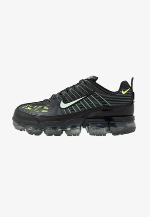 Black athletic shoe with a textured upper, featuring green accents, a rounded toe, and a segmented transparent sole. Subtle logo on side.