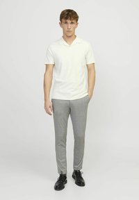 Polo bianco a maniche corte abbinato a pantaloni grigi su misura e scarpe nere. L'outfit presenta un design pulito con una texture morbida.