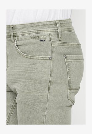 Svijetlozelene traperice s uskim krojem, suptilnim izbljeđivanjem i kontrastnim šavovima. Uključuju prednje i stražnje džepove.