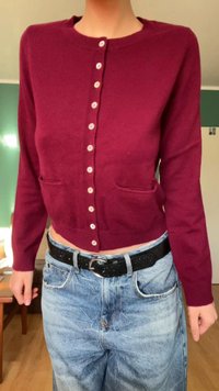 Cardigã curto bordeaux com decote redondo, fecho frontal com botões e dois bolsos. Usado sobre jeans baggy azul claro e cinto preto.
