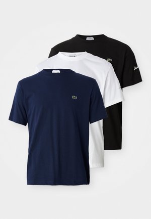 Trys Lacoste trumpių rankovių marškinėlių su apvalia apykakle, mėlynai, balti ir juodi, kiekvienas su mažu krokodilo logotipu ant krūtinės.