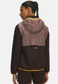 Brown and light brown hooded jacket with a drawstring, featuring an orange accent at the hem and "TRAIL" logo at the back.