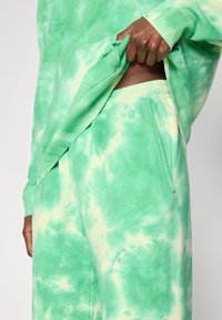 Πράσινο φούτερ με σχέδιο tie-dye και άνετη εφαρμογή, με τσέπη καγκουρό. Το σετ συμπληρώνουν παν τελόνια τζόγκερ με ελαστική μέση και πλαϊνές τσέπες.