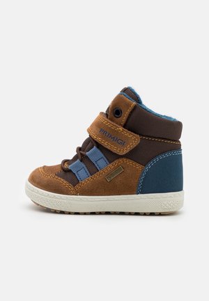 Zapatilla de niño en marrón y azul con correa de velcro, cordones elásticos azules, etiqueta Gore-Tex y suela de goma blanca sobre fondo blanco.