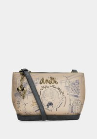 Bolso cruzado beige con base negra, correa negra, charm en forma de corazón y un boceto de una niña de dibujos animados con "Anekke" y dibujos decorativos de estilo urbano.