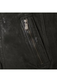 Detail einer schwarzen Lederjacke mit einer Reißverschlusstasche und silbernem Reißverschluss, strukturiertem Oberflächen und sichtbaren Nahtakzenten.
