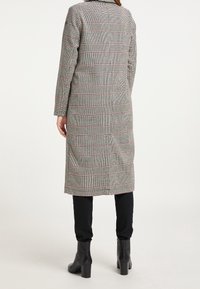 Cappotto a quadri lungo nei toni di grigio, rosso e nero; presenta una linea dritta, maniche lunghe e una fessura centrale sul retro. Abbinato a pantaloni neri aderenti e stivali alla caviglia.
