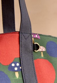 Kangaskassi, jossa on vihreä tausta, punaisia ja sinisiä pyöreitä kuvioita sekä värikkäitä sieniaiheisia kuvia, ja tummansiniset hihnat.
