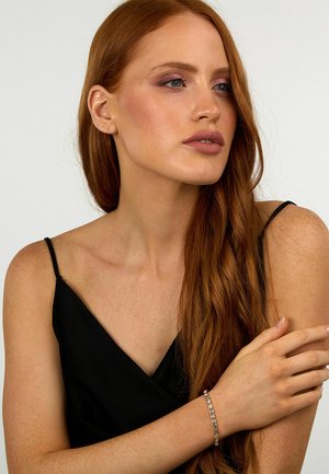 Camisola nera di satin con spalline sottili, modello con lunghi capelli rossi, indossa un braccialetto d'argento con gemme rettangolari trasparenti.