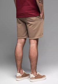 Shorts beiges en mélange de coton, avec des poches latérales, une coupe décontractée et un ourlet visible. Portés avec des baskets marron clair.
