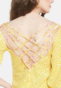 Gelbes Gingham-Oberteil mit ausgefallenem Kreuzrücken-Design aus gemusterten Trägern. Verfügt über eine weiche Textur und einen gewellten Ausschnitt.