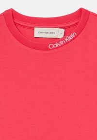 Rosa bomulls T-skjorte med rund hals. Har "Calvin Klein" logo i hvit stikking på kragen. Størrelsesmerke synlig inni.