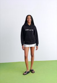 Felpa nera con cappuccio e logo bianco, abbinata a pantaloni corti metallici argento e infradito nere. Tessuto morbido e vestibilità comoda.