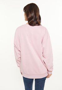 Sweatshirt oversize rosa chiaro con scollatura rotonda e spalle calate, realizzato in tessuto morbido, abbinato a jeans azzurri aderenti.