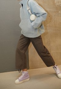 Helles blauer Fleece-Pullover, braune Cargo-Hosen und lavendelgraue, strukturierte High-Top-Sneaker mit weißen Sohlen. Die Accessoires umfassen eine runde weiße Tasche.
