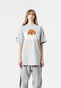 Camiseta gris de gran tamaño con un gráfico de un perro marrón texturizado y letras blancas en negrita que dicen "Black". Corte casual con mangas cortas.