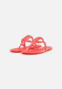 Korallfärgade plasttofflor med en dekorativ utskärningsdesign på remmarna och en slät sula, som har en minimalistisk stil och lätt konstruktion.