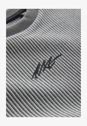 Sivkasta rebraste tkanine z teksturnim vzorcem; vsebuje temno vezeno logotipno akcent. Gladko okroglo ovratnik z kontrastnim obrobo.