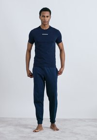 Tumši zils īsām piedurknēm T-krekls ar mazu logotipu uz krūšu daļas, apvienots ar atbilstošiem tumši ziliem treniņbiksēm. Vienkāršs, brīvs piegriezums, mīksts audums.