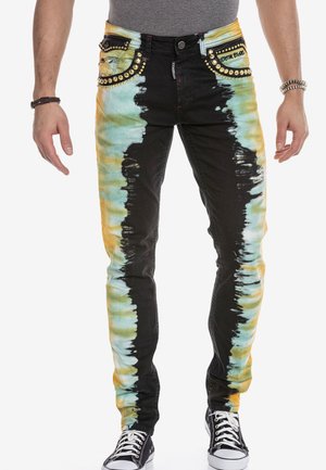 Schwarze Jeans mit Batikmustern in Gelb und Türkis. Mit dekorativen Nieten an den Taschen, slim fit und Kontrastnähten.