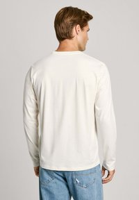 Cremfarbiges Langarm-T-Shirt aus weichem Stoff, mit einem Rundhalsausschnitt und einem schlichten Design. Kombiniert mit hellblauen, zerrissenen Jeans.