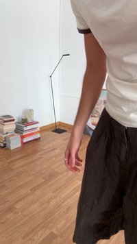 Black linen shorts with a relaxed fit, paired with a light-colored short-sleeve shirt. Background features a stack of books and a floor lamp.