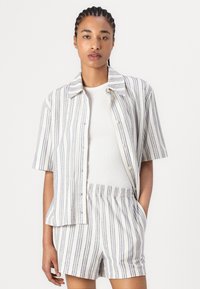 Stripet skjorte og shorts sett i hvitt med blå vertikale striper. Korte ermer, knappelukking foran, og elastisk midje på shorts.
