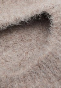 Béžová jemná vlnená tkanina s chlpatou textúrou a mierne melírovaným vzorom. Je prehodená tak, aby ukázala mäkkosť a hĺbku.