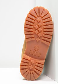Podeszwa buta Timberland w pomarańczowej gumie, charakteryzująca się wyraźnym wzorem bieżnika i logo marki. Cholewka wykonana z naturalnej, brązowej skóry.