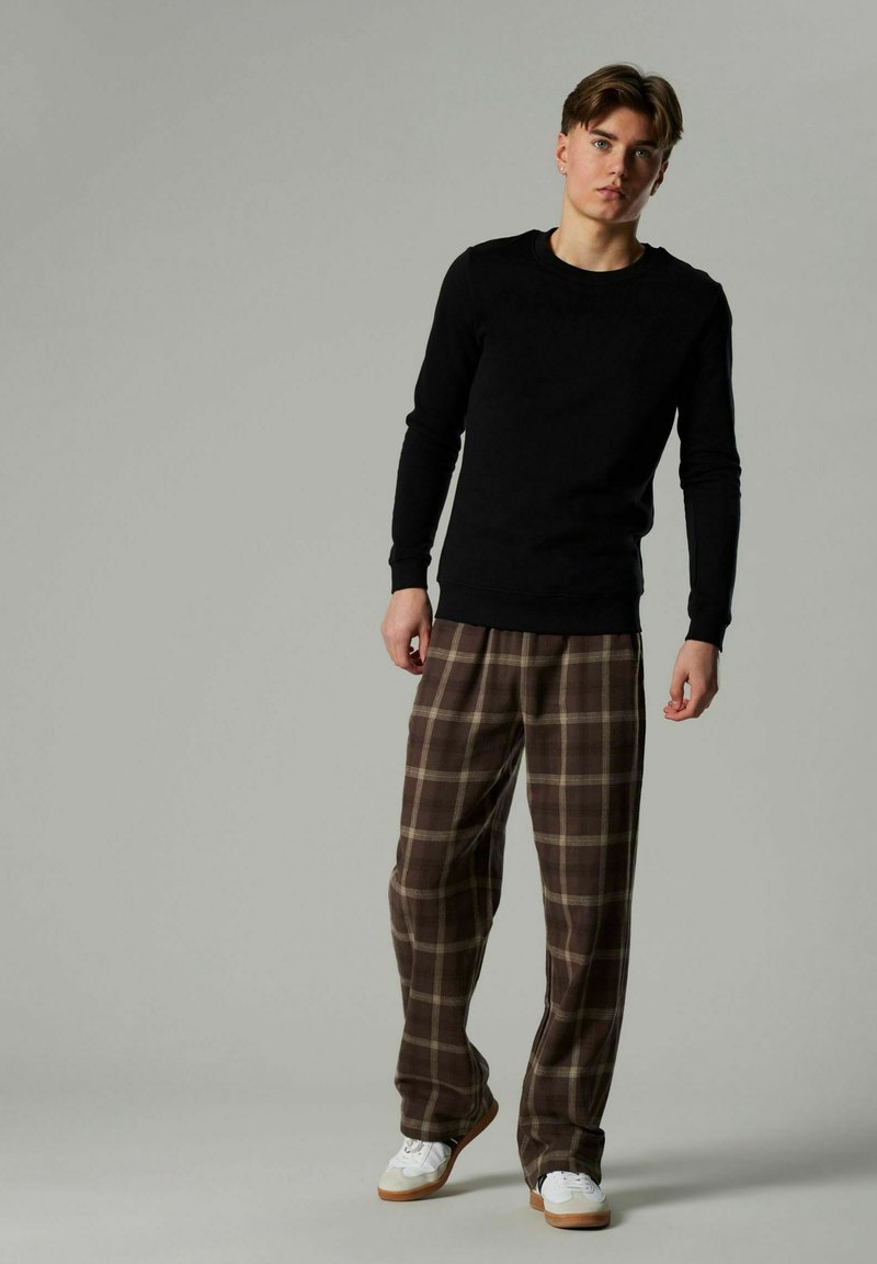 Top negro de manga larga combinado con pantalones de cuadros marrones y beiges, con un corte relajado y zapatillas blancas con suela marrón.
