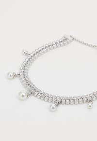 Collier ras du cou en argent avec plusieurs rangées de strass clairs et trois perles blanches pendantes, au fini lisse et avec un fermoir à chaîne.