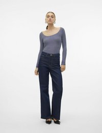 Longsleeve rebrastop v svetlo vijolični barvi, v kombinaciji z visokim pasom temnonosnimi flared kavbojkami. Model nosi črne čevlje s konicami.