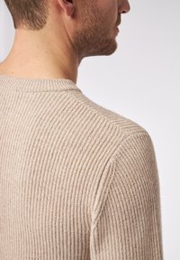 Beiger gerippter Pullover mit Rundhalsausschnitt und strukturiertem Strick. Hat eine schlanke Passform, sichtbare Nähte und einen weichen, gemütlichen Stoff.
