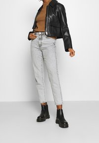 Personne portant une veste en cuir noire courte, un pull côtelé marron, un jean taille haute gris clair et des bottines noires à semelles épaisses.