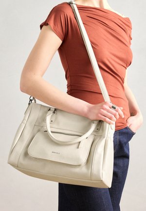 Sac à main en cuir blanc avec des poignées doubles et une bandoulière amovible, doté d'une poche zippée à l'avant et d'une texture lisse. Porté au bras d'une personne.