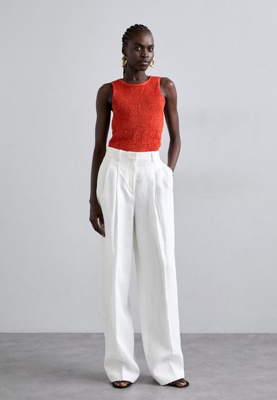 Κόκκινη αμάνικη μπλούζα με ελαστική εφαρμογή, συνδυασμένη με λευκά παντελόνια σε φαρδιά γραμμή. Μαύρες σχετικές σαγιονάρες ολοκληρώνουν την εμφάνιση.