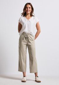 Lichte, kortebloemige witte top met een V-hals; beige, losvallende cargopantalon met twee zijzakken en een elastische tailleband.