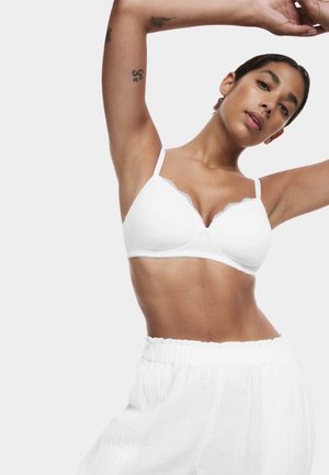 Reggiseno bianco con bordi smerlati, tessuto morbido, spalline regolabili e forma triangolare, abbinato a pantaloni bianchi con trama.