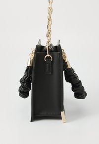 Sac à main en similicuir noir à forme rigide, doté de ferrures dorées, d'une bandoulière chaîne et de poignées souples et froncées.