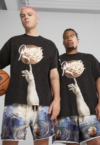 Sorte oversized t-shirts med et basketball-grafik og en hånd, parret med farverige shorts med et virvlende mønster og basketballmotiver.