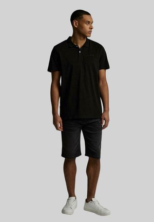 Czarna bawełniana koszulka polo z klasycznym kołnierzykiem, zestawiona z ciemnymi dżinsowymi szortami i białymi sneakersami, o prostym fasonie i regularnym kroju.