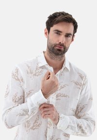 Weißes Leinenhemd mit einem dezenten beigen Blattmuster, langen Ärmeln und einem Button-Down-Kragen. Weicher Stoff und lockere Passform.