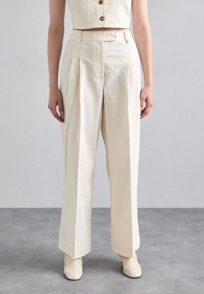 Cream-colored wide-leg pants with a textured fabric, featuring front pleats, a high waist, and a smooth finish. The hem is slightly flared.